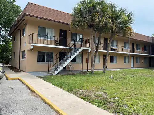 Two story South Daytona apartment building finished in tan stucco with brown trim, an exterior stair and palm trees out front