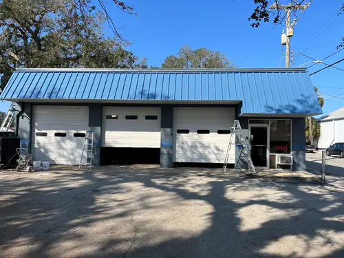 The same Port Orange auto shop after repainting, with a deep blue metal roof, dark grey block columns and white bay doors
