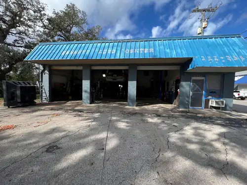 Port Orange auto shop before repainting, with a faded powder blue metal roof and old lettering across the fascia above three open service bays