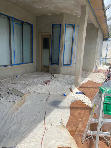 Daytona Beach lanai during prep for painting, with canvas drop cloths over the floor and blue tape masking the window and door frames