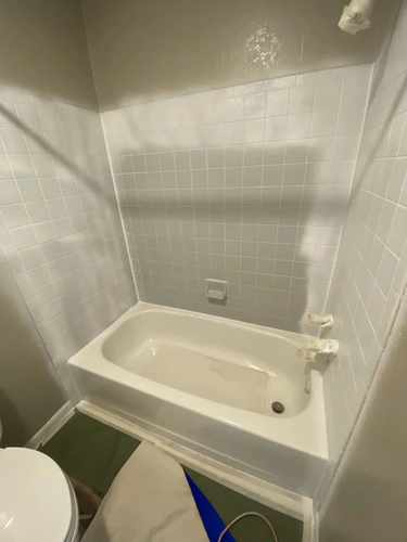 New Smyrna Beach bathtub and tile surround during refinishing, with the tub coated white and the floor covered in paper and drop cloth