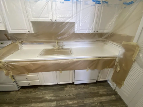 Ormond Beach kitchen during prep for painting, with cabinets and backsplash wrapped in plastic and masking paper along the counter edge