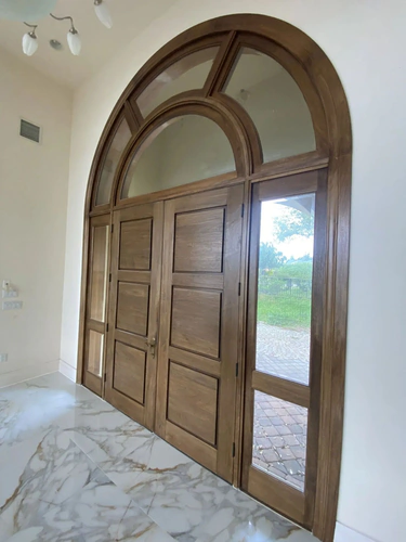 Arched double wood front doors with an arched transom and glass sidelights, stained walnut brown, inside a Daytona Beach home with marble floors