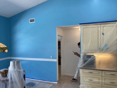 New Smyrna Beach living and kitchen area with freshly painted bright blue walls and white chair rail, cabinets still covered in plastic
