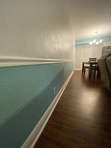 Long Port Orange dining hall painted turquoise below a white chair rail with a white textured wall above and a dining table at the far end