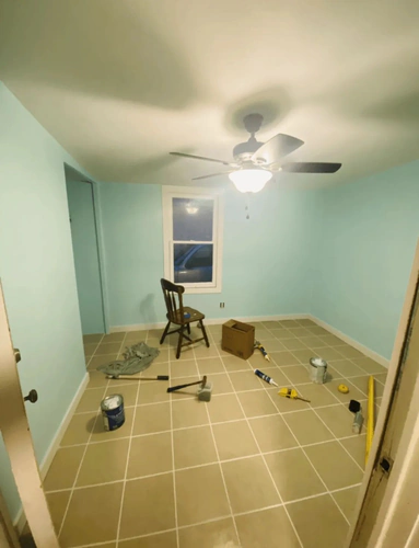 Port Orange living room freshly painted light aqua with white baseboards, a ceiling fan, and painting tools still on the tile floor