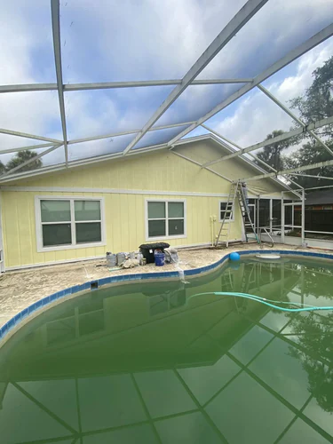 The same Ormond Beach back wall painted pale yellow with white window trim, seen across the pool inside the screen enclosure