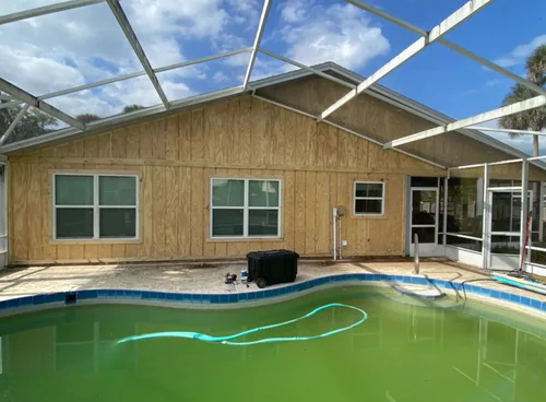 Back of an Ormond Beach home before painting, with bare new wood siding behind a screened pool enclosure