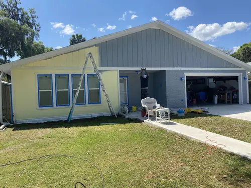 Front of the Ormond Beach home part way through painting, with a yellow body and the original grey gable and garage section not yet painted