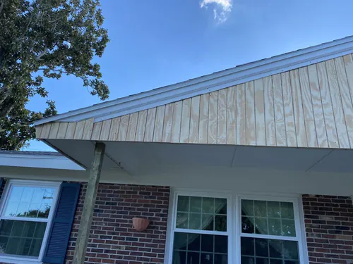 The same New Smyrna Beach porch gable closed in with new bare plywood siding above white soffit and fascia, before primer and paint