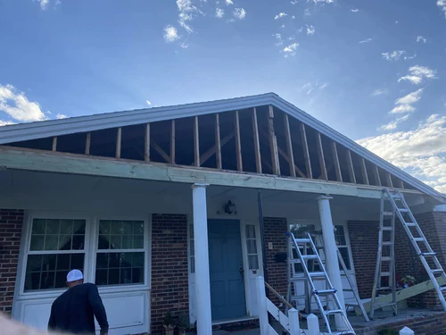 New Smyrna Beach brick home during a remodel, with the front porch gable opened to bare framing and ladders on the porch, not yet painted