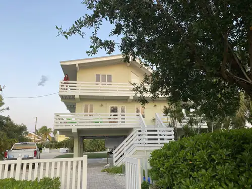 Raised Daytona Beach rental building on pilings painted pale yellow with white railings, balconies and stairs