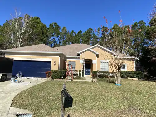 Finished Ormond Beach stucco home painted peach with white trim, a navy garage door and a navy front door under the arched entry