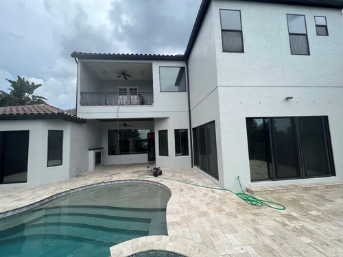 Two story Daytona Beach home with freshly painted white stucco walls around a travertine pool deck