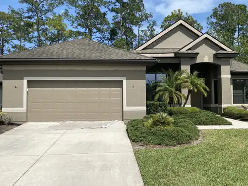 Finished South Daytona stucco home painted taupe grey with white trim around the garage door and windows and palms in the front bed