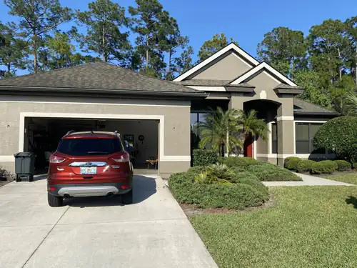 Finished South Daytona home with taupe grey stucco, white trim and a red front door under the entry arch, with a car in the driveway
