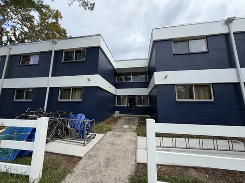 Two story Gainesville student housing building after exterior painting, with navy concrete block walls, white floor line bands and fascia, and a bike rack by the entry walk